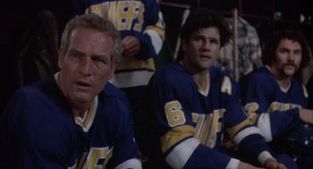 Movie still from “Slap Shot” (1977), directed by George Roy Hill – Two hockey players are sitting in the stands; Close Up shot, Low angle