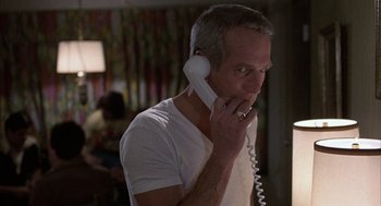 Movie still from “Slap Shot” (1977), directed by George Roy Hill – A man talking on a phone while standing in a room; Close Up shot, Low angle