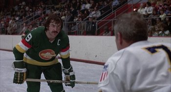 Movie still from “Slap Shot” (1977), directed by George Roy Hill – A man in a green and white hockey uniform; Medium shot, Over the shoulder angle