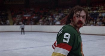 Movie still from “Slap Shot” (1977), directed by George Roy Hill – A man in a green and red hockey uniform; Medium shot, Low angle