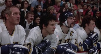 Movie still from “Slap Shot” (1977), directed by George Roy Hill – A group of men sitting on top of a hockey rink; Medium shot, Low angle