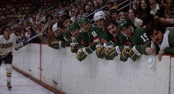 Movie still from “Slap Shot” (1977), directed by George Roy Hill – A group of hockey players on the side of a wall; Wide shot, High angle