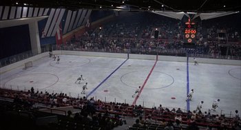 Movie still from “Slap Shot” (1977), directed by George Roy Hill – A hockey game is being played in an indoor arena; Extreme Wide shot, High angle