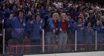 Movie still from “Slap Shot” (1977), directed by George Roy Hill – A group of people standing on top of a hockey rink; Wide shot, High angle