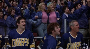 Movie still from “Slap Shot” (1977), directed by George Roy Hill – A group of men and women in the bleachers at an ice hockey game; Medium shot, Low angle