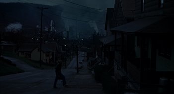 Movie still from “Slap Shot” (1977), directed by George Roy Hill – A person riding a skate board on a city street at night; Extreme Wide shot, High angle