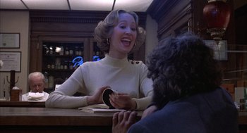 Movie still from “Slap Shot” (1977), directed by George Roy Hill – A woman sitting at a table with a cup of coffee; Medium shot, Over the shoulder angle