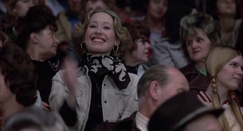 Movie still from “Slap Shot” (1977), directed by George Roy Hill – A woman in a crowd of people wearing a black and white scarf; Close Up shot, Low angle
