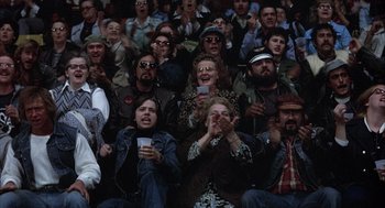 Movie still from “Slap Shot” (1977), directed by George Roy Hill – A group of people sitting in a crowd clapping; Wide shot, High angle