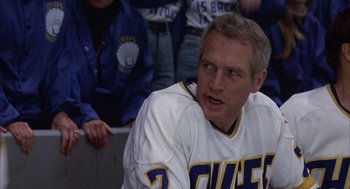 Movie still from “Slap Shot” (1977), directed by George Roy Hill – A man in a hockey uniform sitting in front of a crowd of people; Medium shot, Low angle