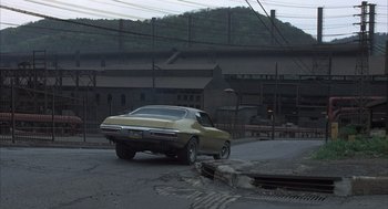 Movie still from “Slap Shot” (1977), directed by George Roy Hill – An old car parked on the side of the road; Extreme Wide shot, High angle