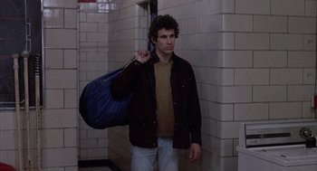 Movie still from “Slap Shot” (1977), directed by George Roy Hill – A young man holding a bag in a hallway; Medium shot, High angle