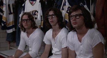 Movie still from “Slap Shot” (1977), directed by George Roy Hill – A group of young men sitting next to each other wearing glasses; Medium shot, High angle