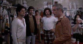 Movie still from “Slap Shot” (1977), directed by George Roy Hill – A group of men standing in a room; Medium shot, Over the shoulder angle