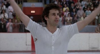 Movie still from “Slap Shot” (1977), directed by George Roy Hill – A man in a white shirt is on the ice; Medium shot, Low angle