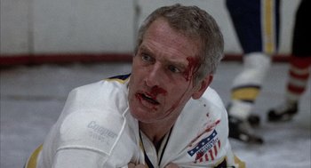 Movie still from “Slap Shot” (1977), directed by George Roy Hill – A hockey player with blood all over his face; Close Up shot, Low angle