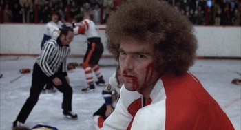 Movie still from “Slap Shot” (1977), directed by George Roy Hill – A hockey player with blood all over his face; Close Up shot, Low angle