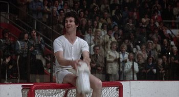 Movie still from “Slap Shot” (1977), directed by George Roy Hill – A man sitting on top of a hockey net; Medium shot, Low angle