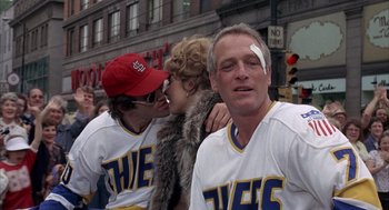 Movie still from “Slap Shot” (1977), directed by George Roy Hill – A couple of people that are standing in the street; Medium shot, Over the shoulder angle