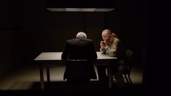 Movie still from “Slasher” (2016), created by Aaron Martin – Two people sitting at a table in a dark room; Medium shot, Over the shoulder angle