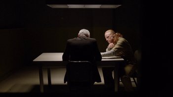 Movie still from “Slasher” (2016), created by Aaron Martin – Two men sitting at a table in a dark room; Medium shot, Over the shoulder angle