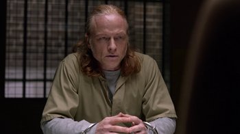 Movie still from “Slasher” (2016), created by Aaron Martin – A man with long blonde hair sitting in a jail cell; Close Up shot, Over the shoulder angle