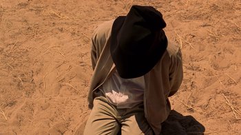 Movie still from “Breaking Bad” (2008), created by Vince Gilligan – A man with a black hat is kneeling in the sand; Close Up shot, High angle