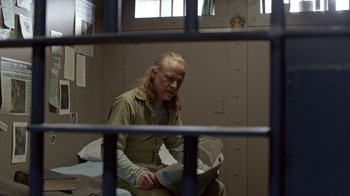 Movie still from “Slasher” (2016), created by Aaron Martin – A man sitting on a bed inside of a jail cell; Medium shot, Over the shoulder angle