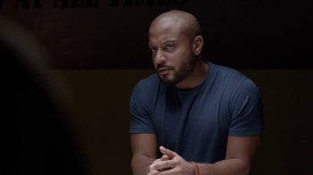 Movie still from “Slasher” (2016), created by Aaron Martin – A man with a shaved head is sitting in a dark room; Close Up shot, Over the shoulder angle