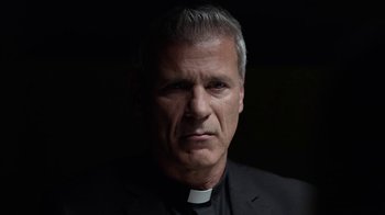Movie still from “Slasher” (2016), created by Aaron Martin – A man wearing a priest's collar and a black suit; Close Up shot, Low angle