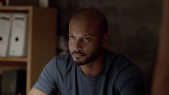 Movie still from “Slasher” (2016), created by Aaron Martin – A man with a shaved head sitting in front of a brick wall; Close Up shot, Over the shoulder angle