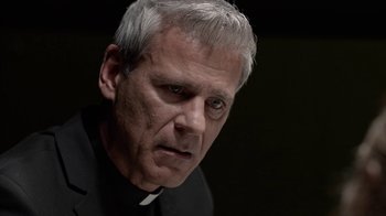 Movie still from “Slasher” (2016), created by Aaron Martin – A man in a priest's outfit stares into the camera; Close Up shot, Over the shoulder angle