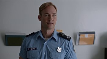 Movie still from “Slasher” (2016), created by Aaron Martin – A man in a blue uniform is smiling for the camera; Close Up shot, Over the shoulder angle