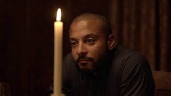 Movie still from “Slasher” (2016), created by Aaron Martin – A man sitting in front of a lit candle; Close Up shot, Over the shoulder angle
