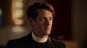 Movie still from “Slasher” (2016), created by Aaron Martin – A person wearing a suit and wearing a priest's collar; Close Up shot, Low angle