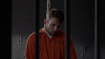 Movie still from “Slasher” (2016), created by Aaron Martin – A man in an orange prison uniform in front of a jail cell; Medium shot, High angle