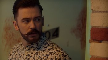 Movie still from “Slasher” (2016), created by Aaron Martin – A man with a beard and mustache is looking to his left; Close Up shot, Over the shoulder angle