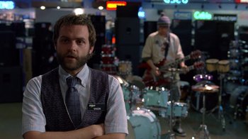 Movie still from “Breaking Bad” (2008), created by Vince Gilligan – A man with a beard is standing in front of some drums; Medium shot, Over the shoulder angle