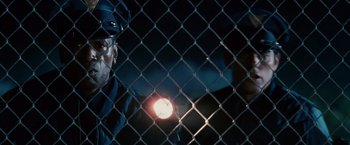 Movie still from “Spider-Man 3” (2007), directed by Sam Raimi – A man holding a flashlight behind a chain link fence at night; Close Up shot, Low angle