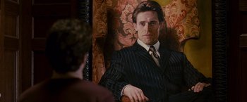 Movie still from “Spider-Man 3” (2007), directed by Sam Raimi – A man in a suit sitting in a chair; Medium shot, Over the shoulder angle