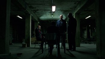 Movie still from “Breaking Bad” (2008), created by Vince Gilligan – A group of men sitting around a table in a dark room; Wide shot, High angle