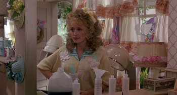 Movie still from “Steel Magnolias” (1989), directed by Herbert Ross – A woman sitting in front of a table with hair products on top of it; Medium shot, Over the shoulder angle