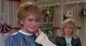 Movie still from “Steel Magnolias” (1989), directed by Herbert Ross – A young woman with blonde hair is crying in front of another young woman; Close Up shot, Over the shoulder angle