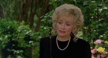 Movie still from “Steel Magnolias” (1989), directed by Herbert Ross – A woman with blonde hair wearing a black shirt and pearls; Close Up shot, Over the shoulder angle
