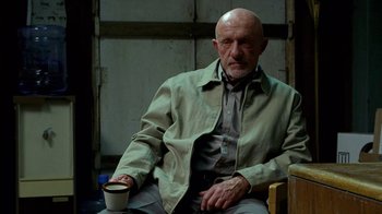Movie still from “Breaking Bad” (2008), created by Vince Gilligan – An older man sitting on a chair holding a coffee cup; Medium shot, Low angle