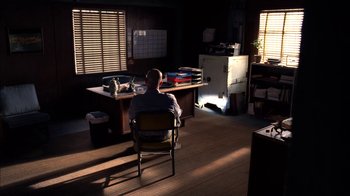 Movie still from “Breaking Bad” (2008), created by Vince Gilligan – A man sitting in a chair in front of a desk in a room; Wide shot, High angle