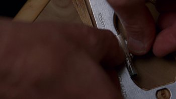 Movie still from “Breaking Bad” (2008), created by Vince Gilligan – A person using a pair of scissors to cut a piece of wood; Extreme Close Up shot, Overhead angle