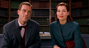 Movie still from “Stuart Little” (1999), directed by Rob Minkoff – A man and a woman sitting next to each other in front of bookcases; Medium shot, Low angle