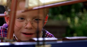 Movie still from “Stuart Little” (1999), directed by Rob Minkoff – A young boy wearing glasses looking at the camera through a window; Close Up shot, Over the shoulder angle