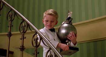 Movie still from “Stuart Little” (1999), directed by Rob Minkoff – A young boy in a white lab coat holding a silver globe; Medium shot, Low angle